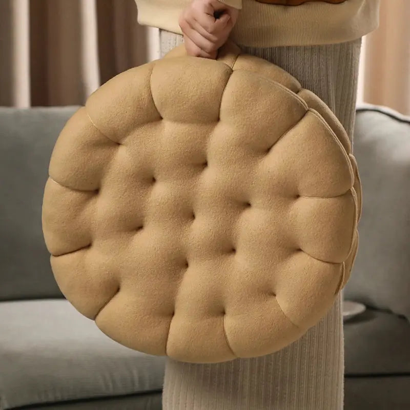 biscuit shaped plush almond beige cushion held by a person in a neutral setting