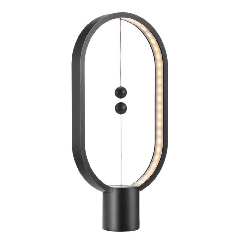 Black LED magnetic table lamp with suspended magnetic sphere switch creating ambient warm lighting on a white background
