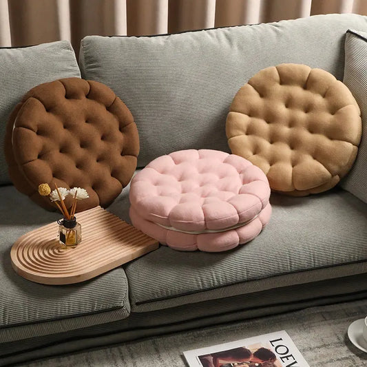 Cute biscuit shaped plush cushion in three colours - strawberry pink, chocolate coffee, and almond beige, soft cartoon cookie pillow for home decor on a grey sofa with a small wooden table.
