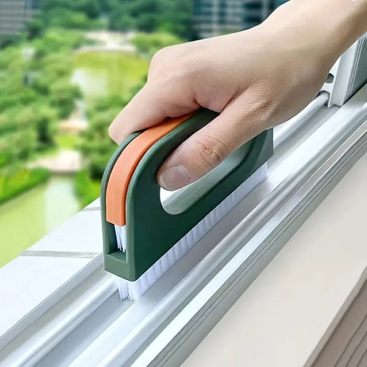 Hand using a window cleaning brush with a green handle to clean a window base.