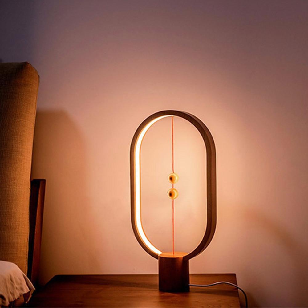 Modern LED magnetic table lamp with suspended magnetic sphere switch creating ambient warm lighting on a wooden surface against a soft pink wall.