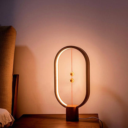 Modern LED magnetic table lamp with suspended magnetic sphere switch creating ambient warm lighting on a wooden surface against a soft pink wall.