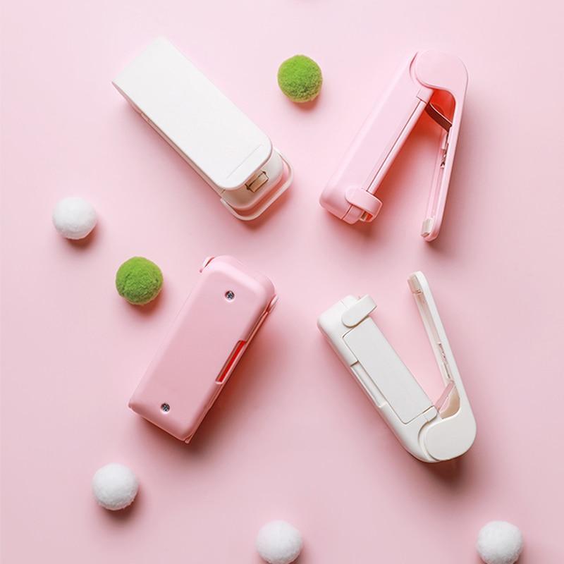 Pink and white Mini heat bag sealer devices on a pink background with decorative items.