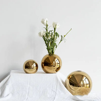 Luxury gold spherical vases with a white flower arrangement on a white surface.