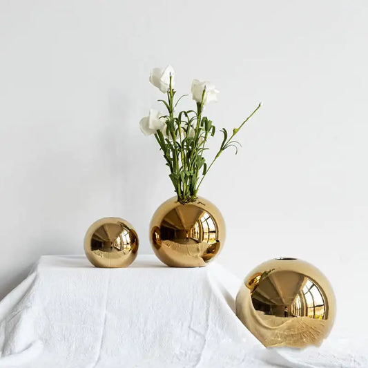 Luxury gold spherical vases with a white flower arrangement on a white surface.