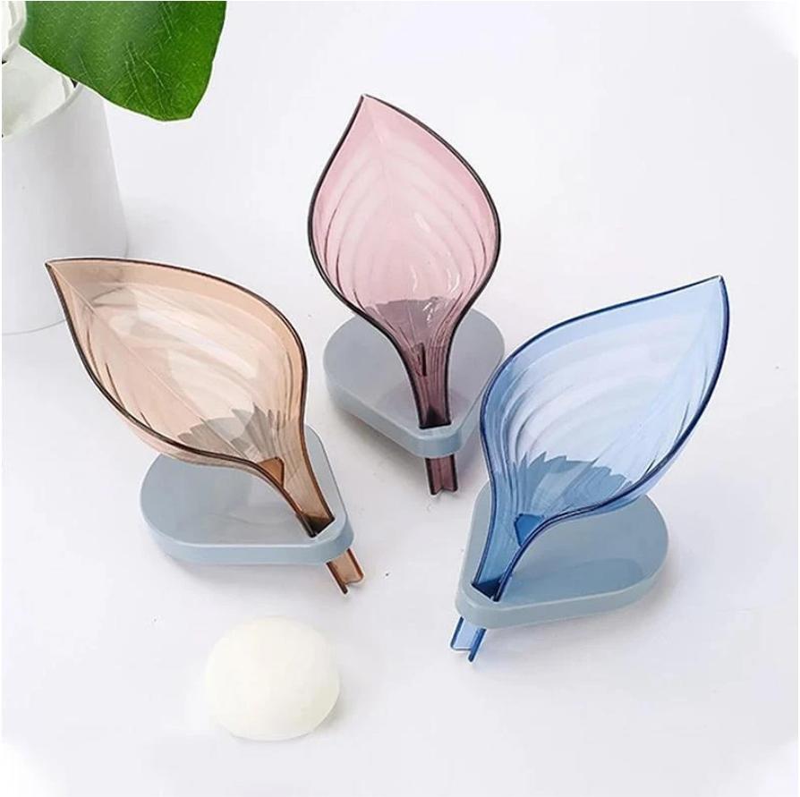 Three leaf shaped soap strainers in pink, blue, and beige on a white background.